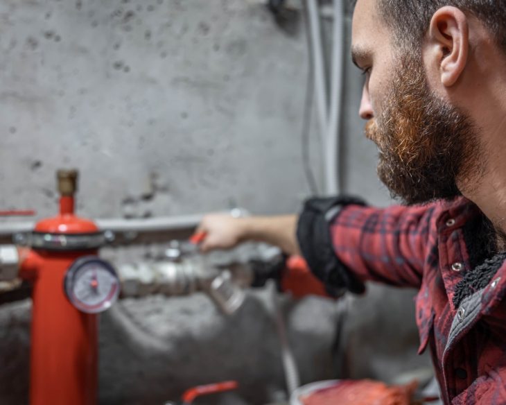 The man looks at the expansion tank, faucet, pipes, valve, pressure meter, copy space.